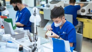 Workers in blue scrubs meticulously craft dental prosthetics in a laboratory.