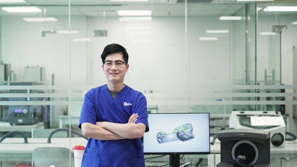 A person in a blue uniform stands in a lab with dental equipment.