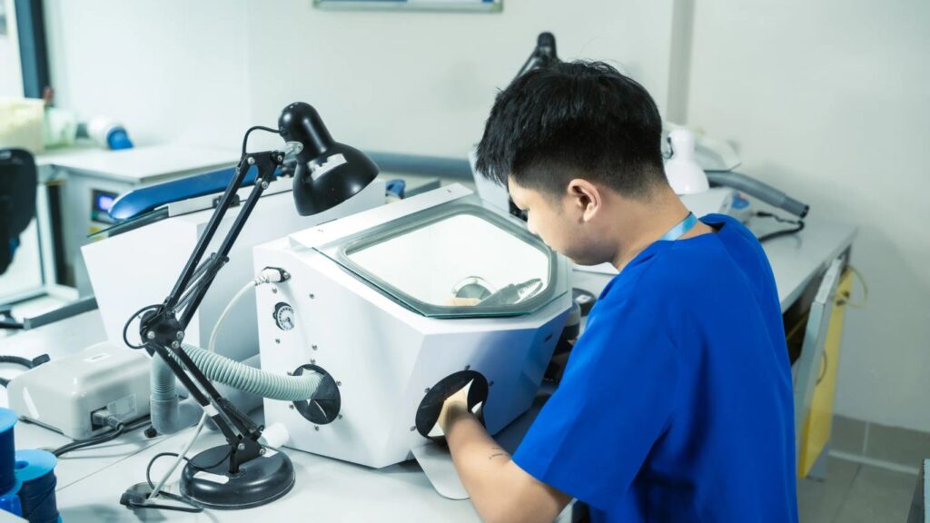 A person works with a dental lab sandblaster machine.