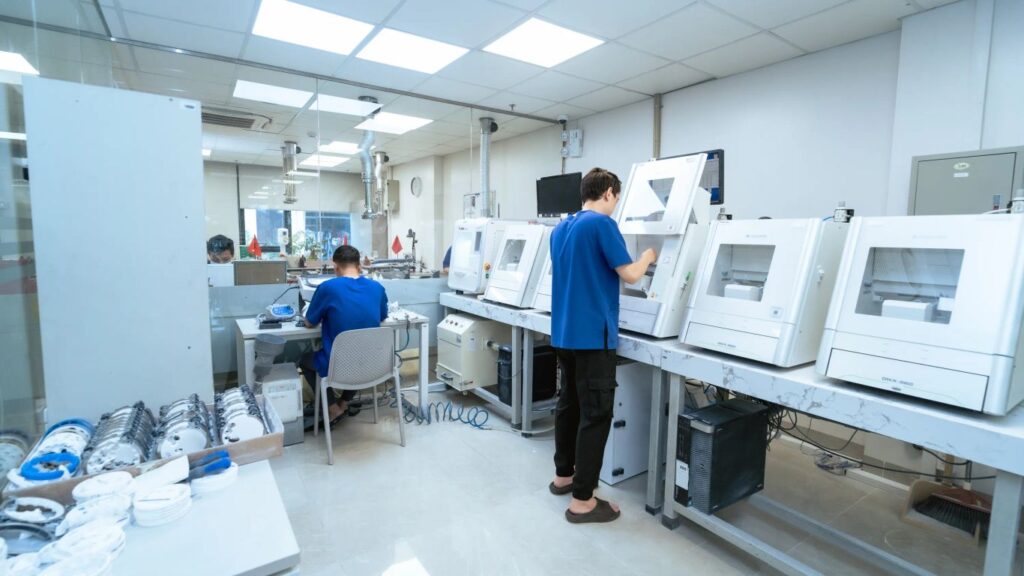 Workers in a lab with dental milling machines and equipment.