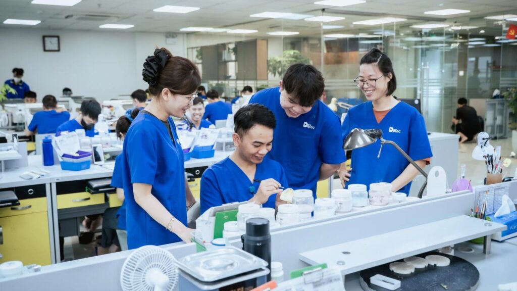 People in blue scrubs working at dental lab benches with equipment.