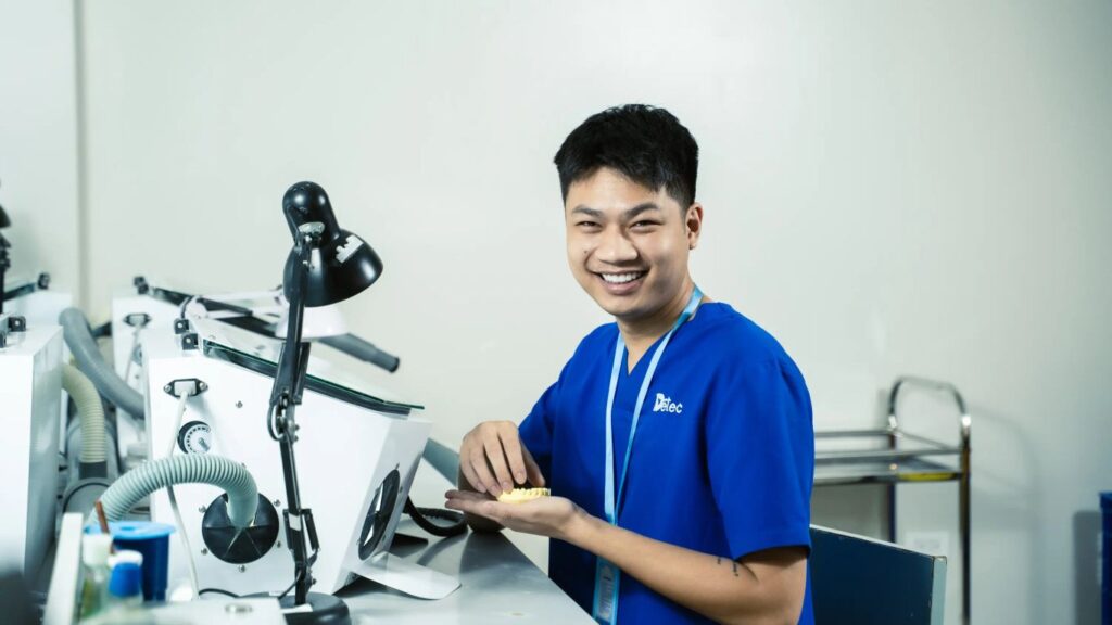 A person in a blue uniform works on a dental prosthesis in a lab.