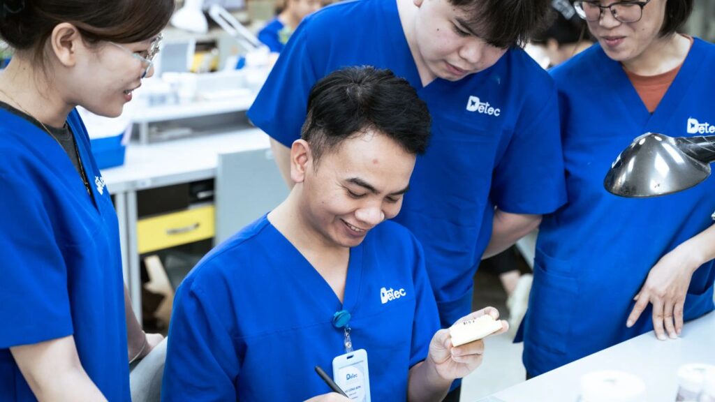 People in blue scrubs working on dental prosthetics in a lab.